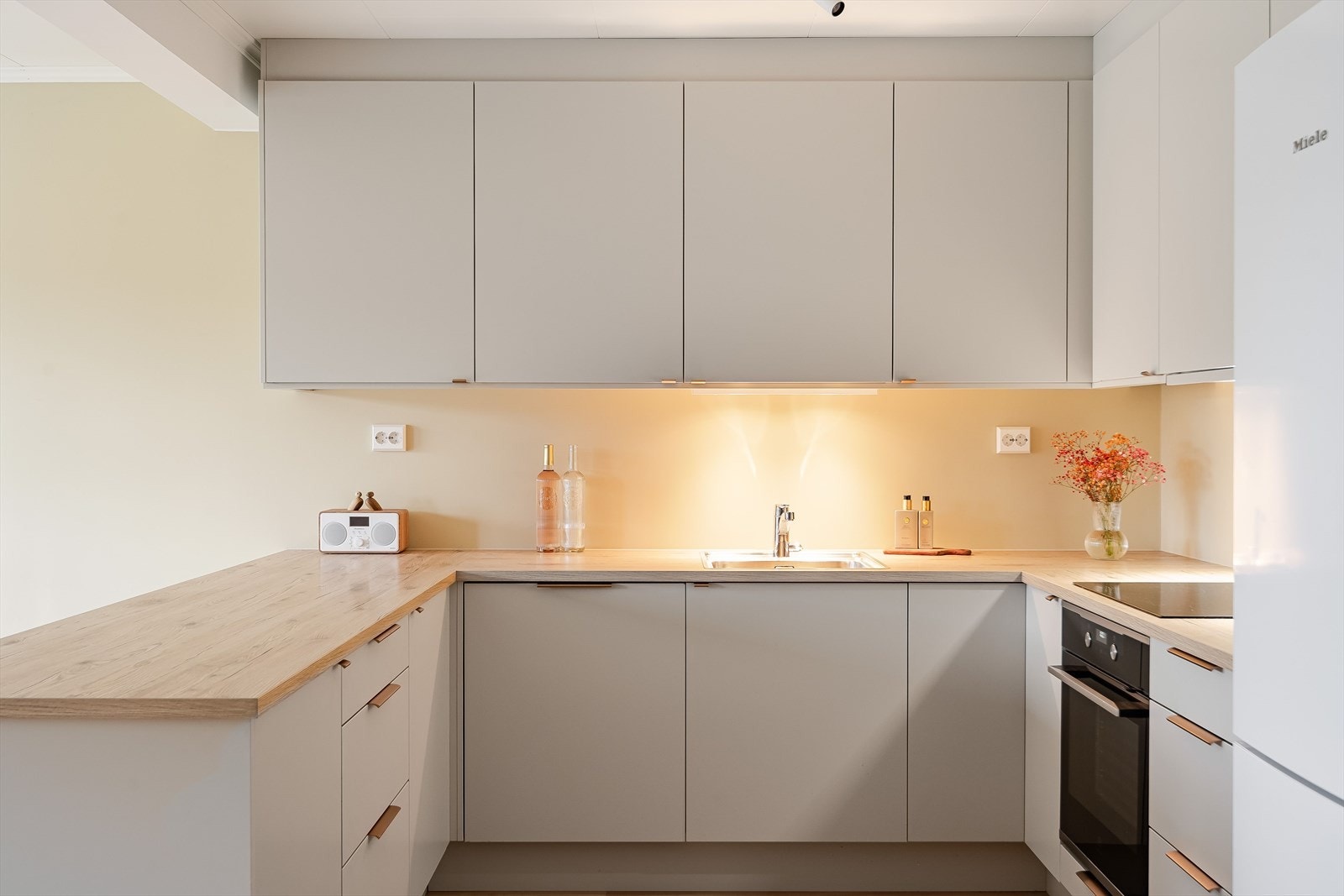 Innredningen har glatte fronter i en lys, tidløs farge og laminert benkeplate med nedfelt oppvaskkum. Praktisk med belysning under de takhøye overskapene. Galleribilde