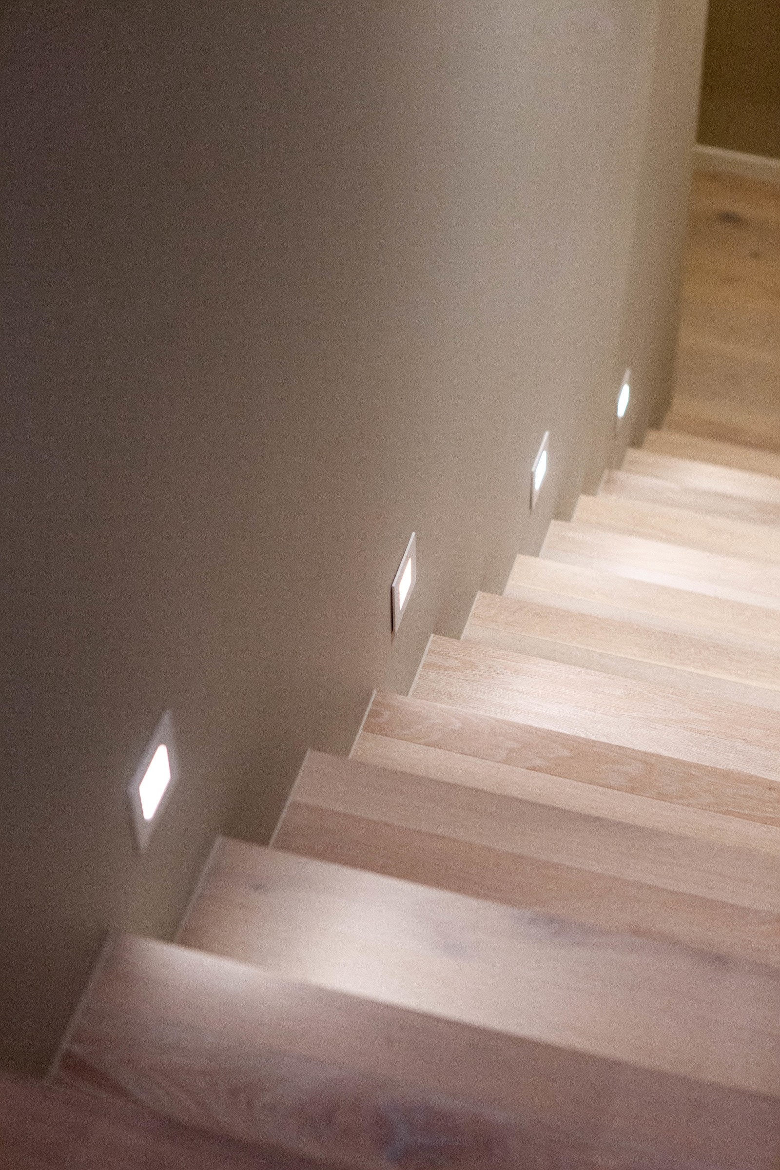 Trappen er pent oppusset med lyse eiketrinn, innfelt trappebelysning i vegg og tett rekkverk mot stuen. Galleribilde