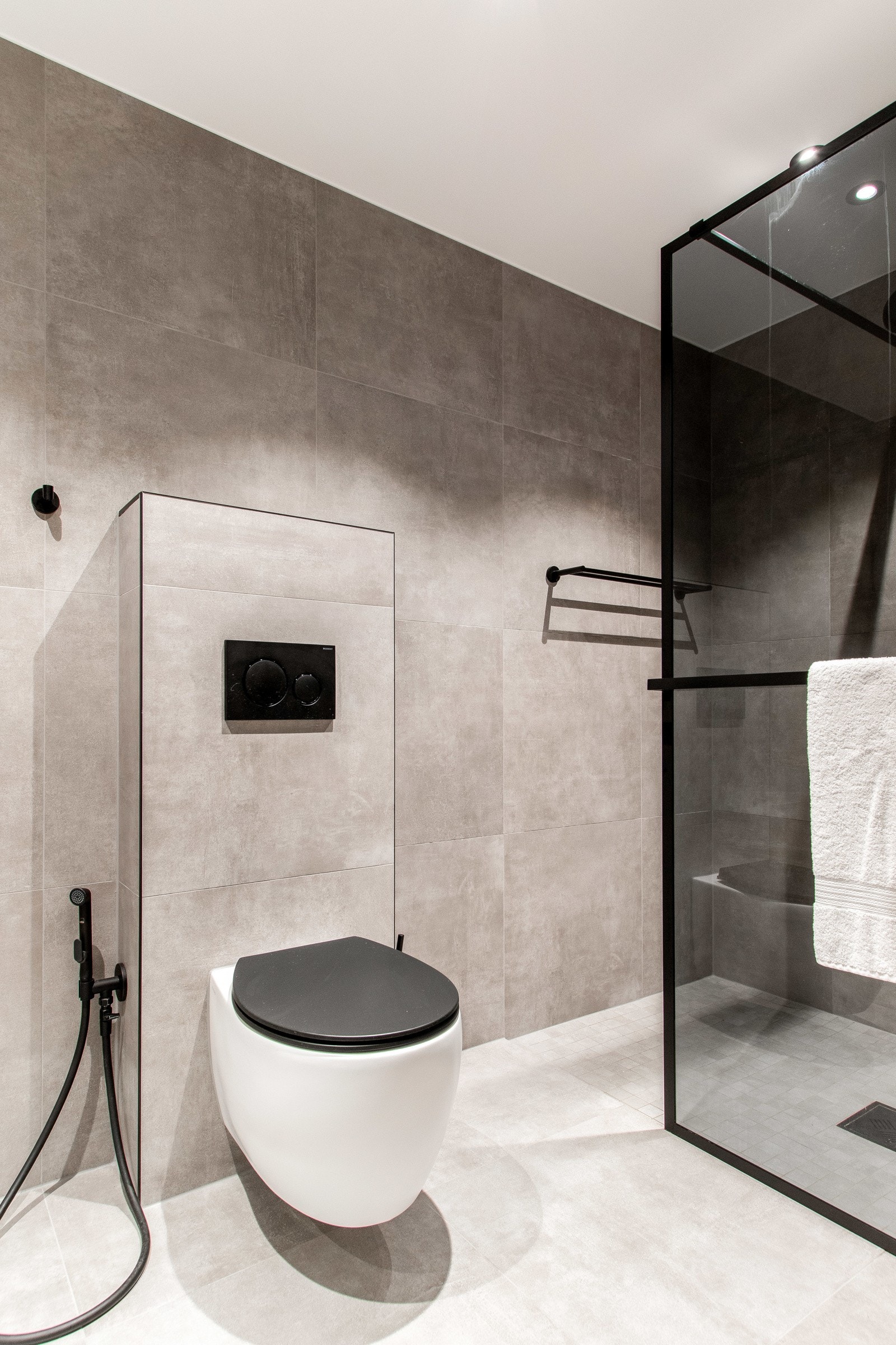 Gulv og vegger er belagt med gråbeige fliser i betongmønster, himlingen er hvitmalt med downlights og det er varmekabler i gulvet. Galleribilde