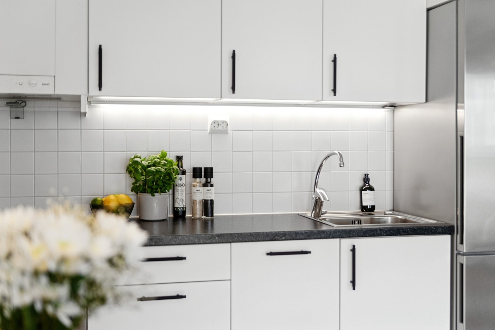 Kjøkkenet har hvite, glatte fronter, takhøye skap og koksgrå benkeplate med nedfelt vaskekum i stål. Galleribilde