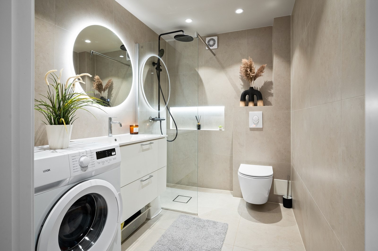 Lekkert og moderne baderom fra 2024 med stilren utførelse, flislagte overflater og vannbåren gulvvarme. Nedsenket dusjsone med glassdører, vegghengt toalett og praktisk servantinnredning gir et rent og funksjonelt uttrykk. Galleribilde