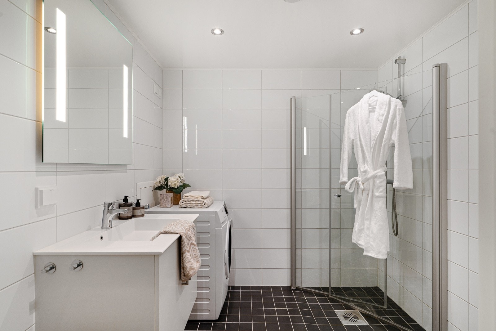 Badet er på romslige 4,9 kvm og er pent flislagt. Rommet er godt opplyst med downlights i tak samt den integrerte belysningen i speilet over servanten. Galleribilde