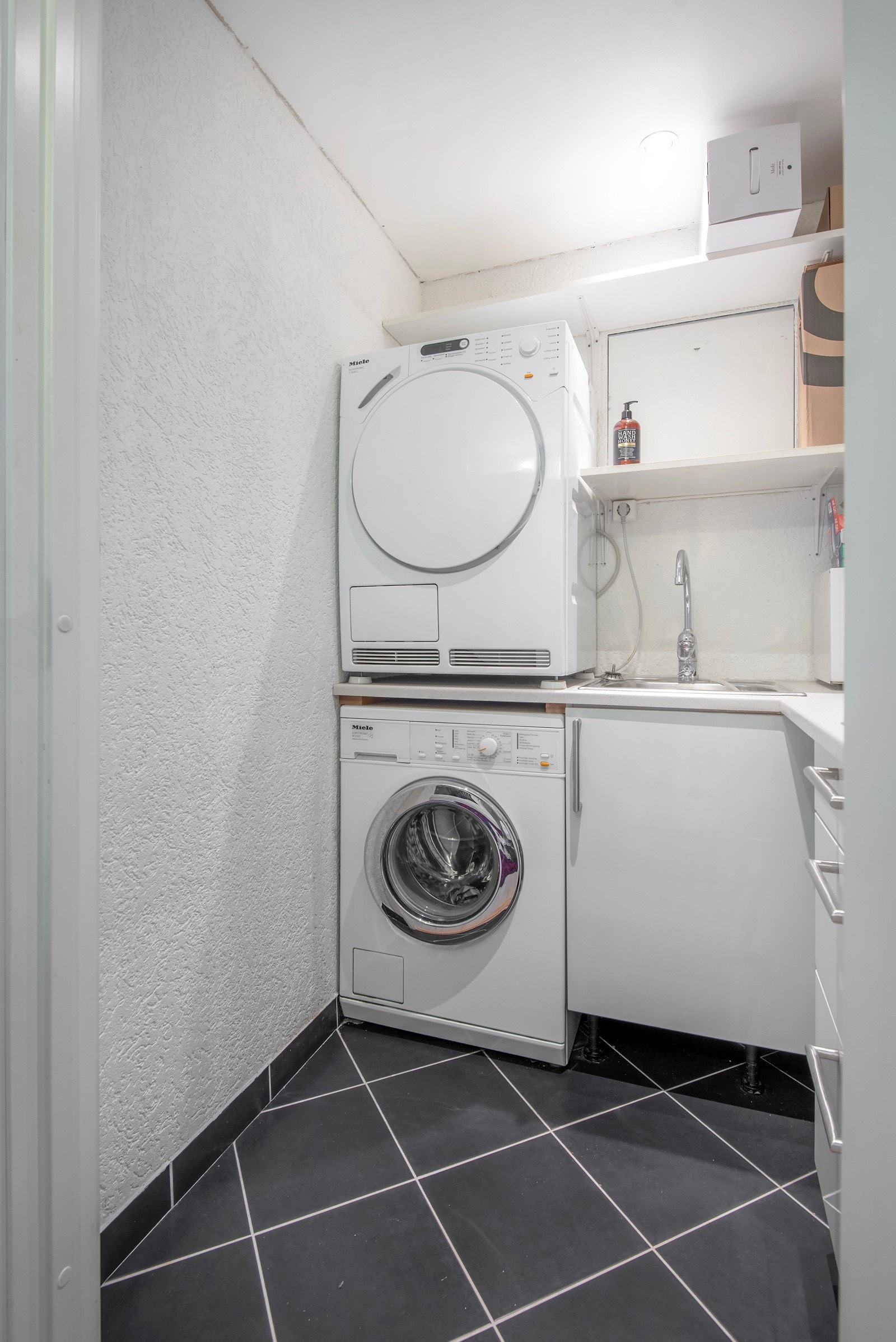 Separat vaskerom med flislagt gulv og elektriske varmekabler. Innredet med innredning med hvite høyglans fronter, laminat benkeplate med stålskyllekum, opplegg for vaskemaskin og tørketrommel. Galleribilde