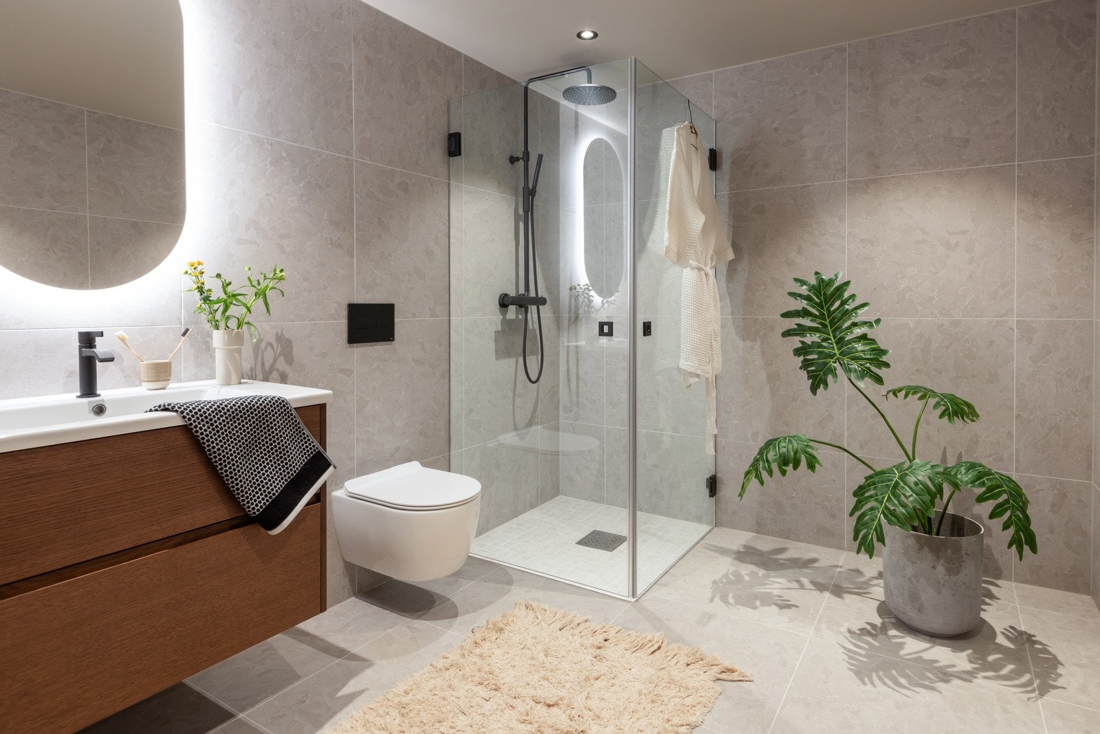 Badet i underetasjen er romslig og holder samme gjennomførte stil som de øvrige badene i boligen, med delikate beige-tonede fliser. Innredningen består av servant med underskuffer, dusjhjørne med regnfallsdusj og vegghengt toalett. Galleribilde