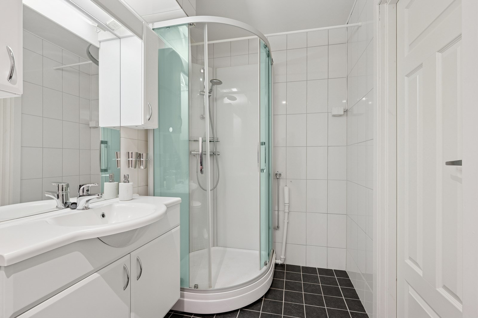 Lyst, flislagt baderom utstyrt med innredning med heldekkende servant, høyskap og dusjkabinett. Galleribilde