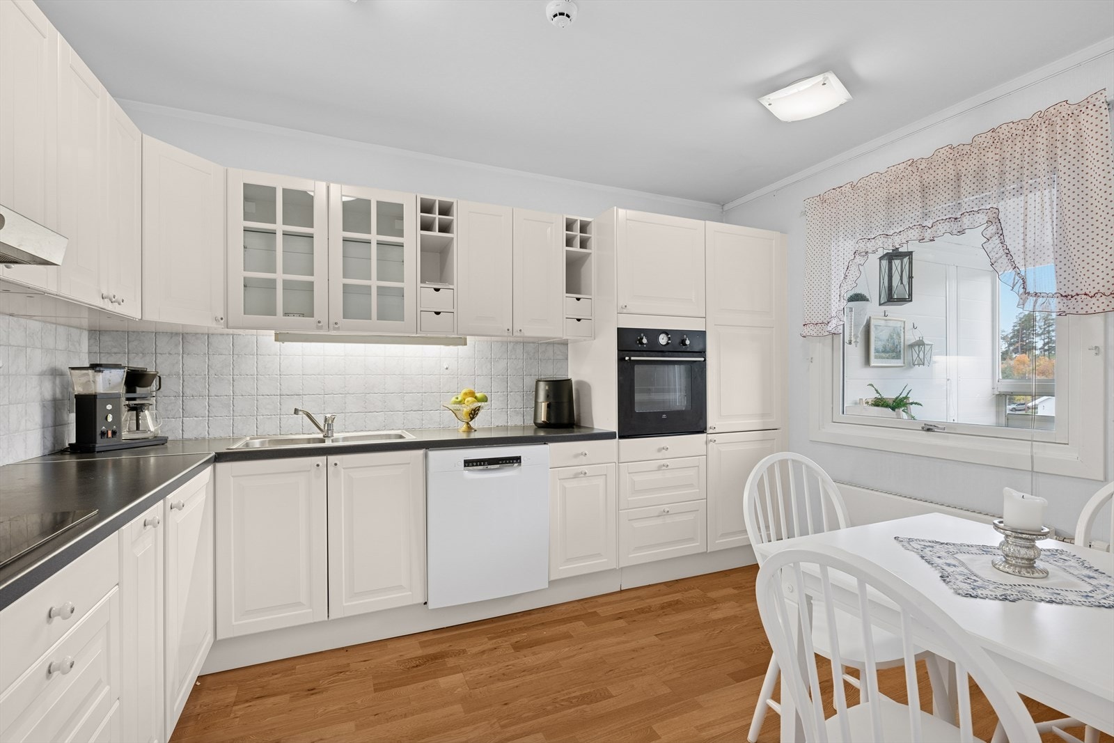 Lys kjøkkeninnredning med profilerte fronter, laminat benkeplate, nedfelt stål dobbelkum og fliser på bakvegg. Galleribilde