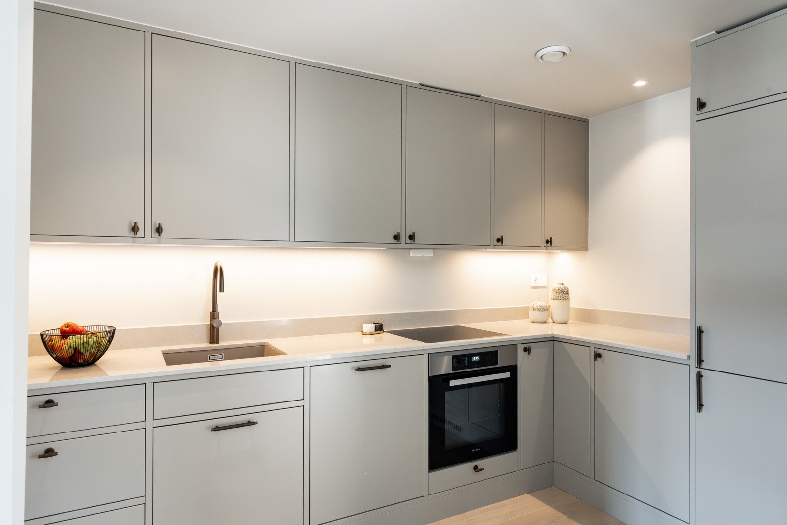 Innredningen har glatte fronter og en stilren kompositt benkeplate som gir både funksjonalitet og et moderne uttrykk. Her finner man integrerte hvitevarer som kjøl-/fryseskap, oppvaskmaskin, induksjonstopp og stekeovn. Galleribilde