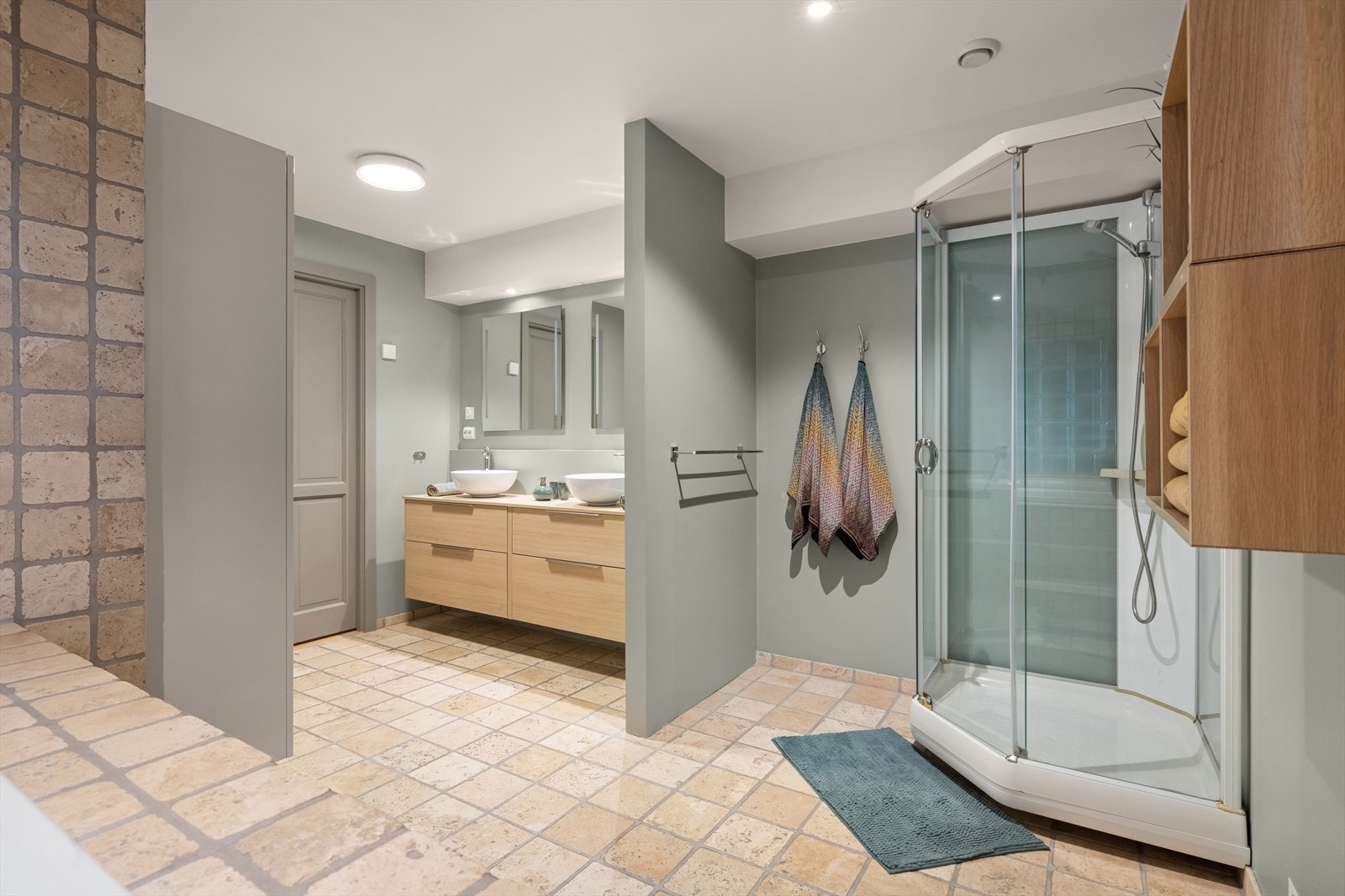 Rommet er utstyrt med veggmontert toalett, dusjkabinett, dobbelservant, innmurt badekar, innredning og speil Galleribilde