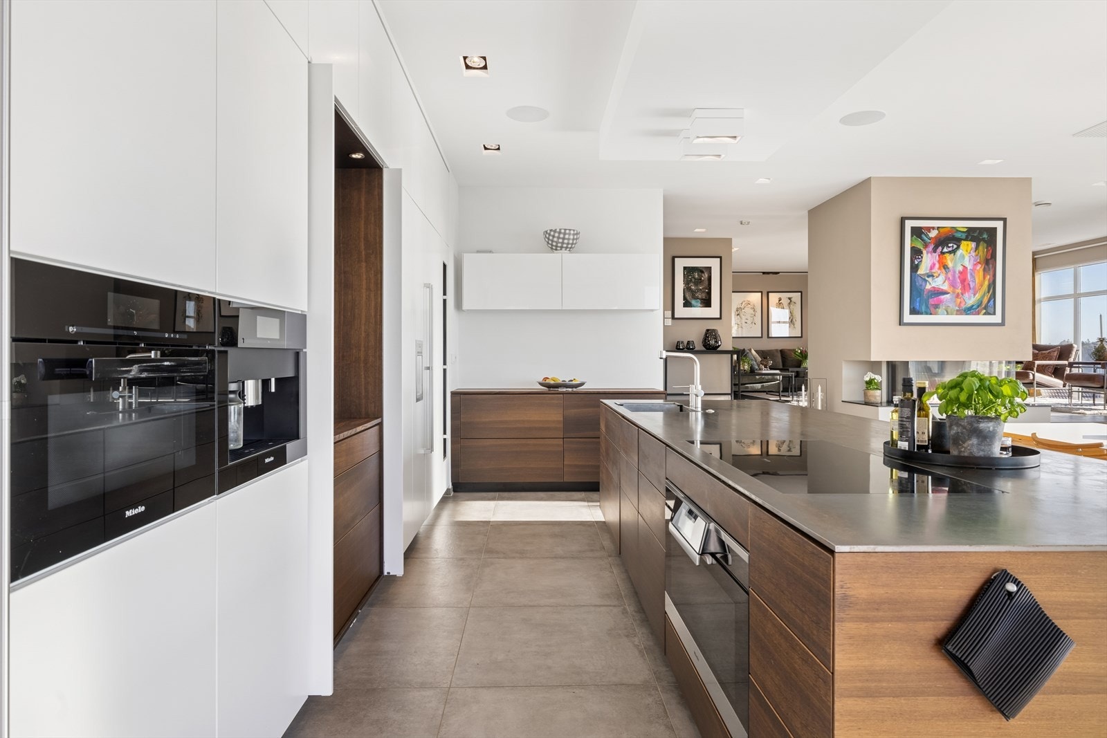 Stor kjøkkenøy med 90 cm bred stekeovn, platetopp og servant er plassert for en sosial utforming. Midtskapet kan lukkes med skjulte fronter Galleribilde