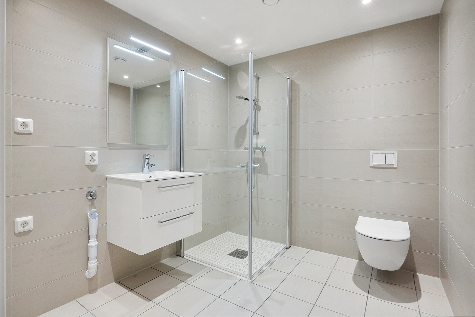 Badet har delikate store fliser, hvit innredning og downlights i tak. Galleribilde