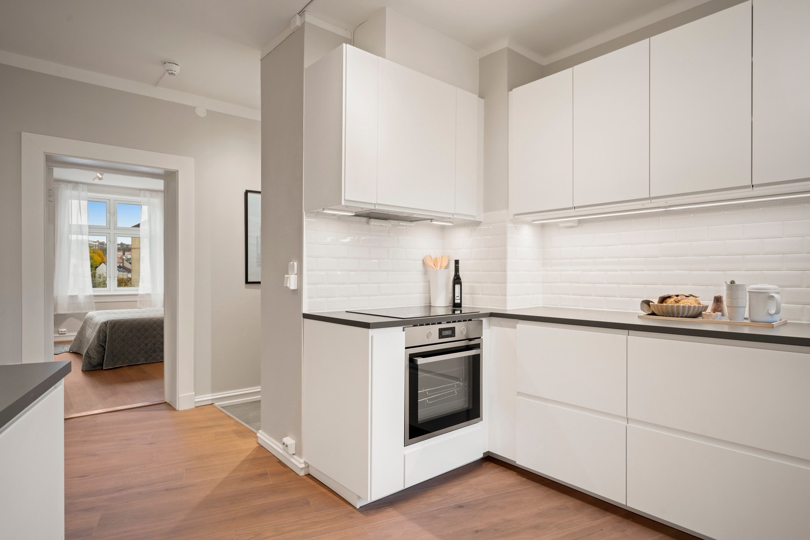 Integrerte hvitevarer bestående av stekeovn, nedfelt induksjonstopp, oppvaskmaskin og nisje for frittstående kjøl/frys. Galleribilde