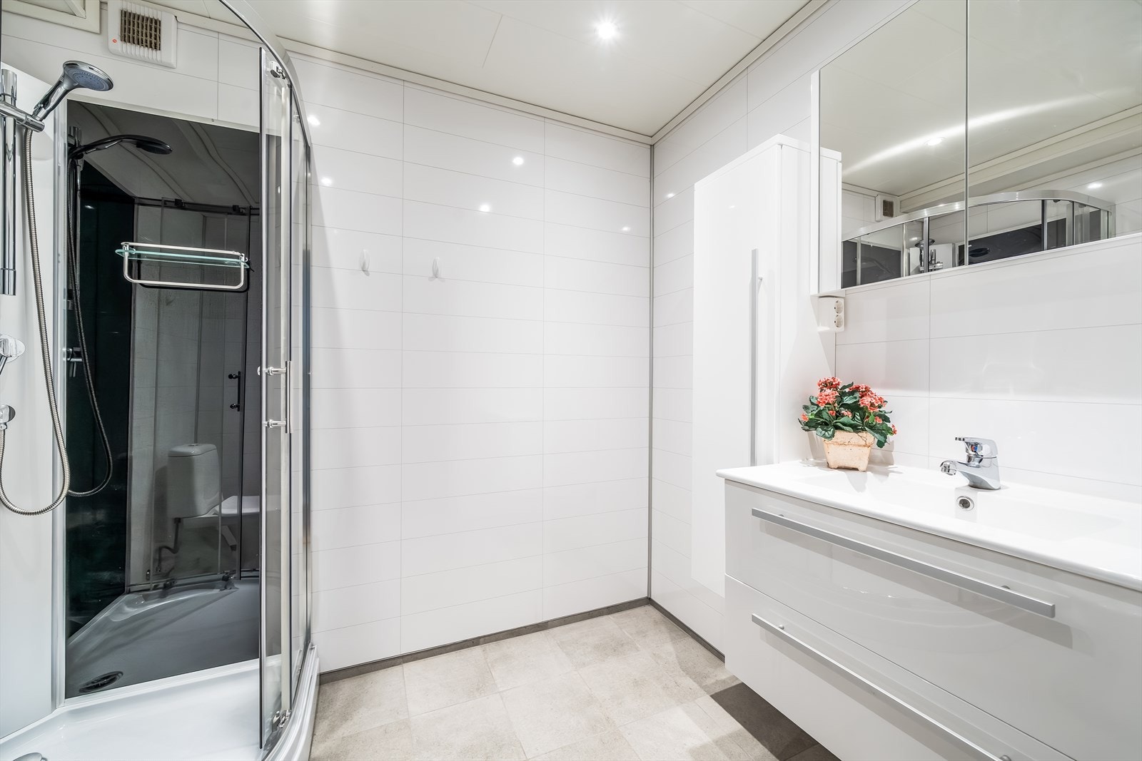 Pent bad med fliser på gulv og baderomsplater på vegg. Innredet med baderomsinnredning, toalett, dusjkabinett og opplegg til vaskemaskin. Galleribilde