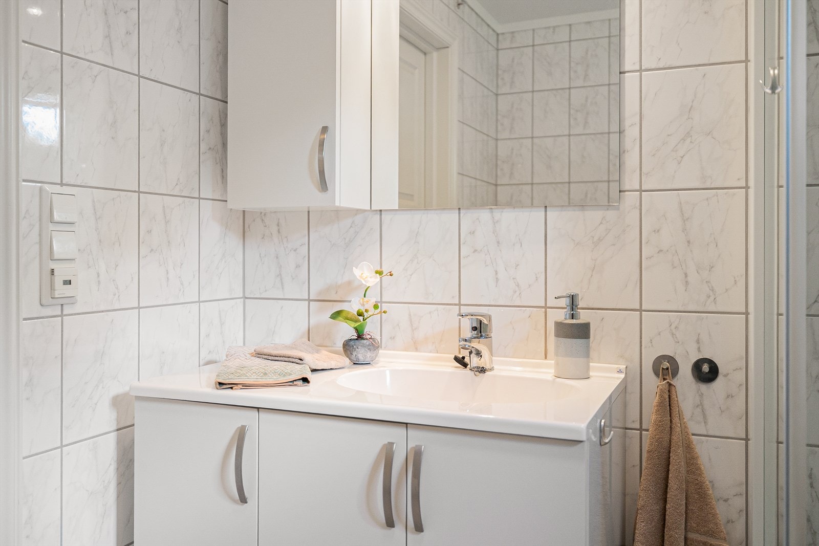 Rommet er utstyrt med en praktisk og stilfull innredning, inkludert en nedfelt servant som gir et moderne uttrykk, samt toalett og dusjvegger/hjørne for optimal utnyttelse av plass. Det er også opplegg for vaskemaskin, noe som gir ekstra funksjonalitet. Galleribilde