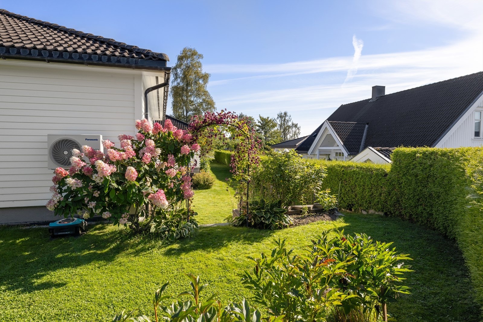 Velstelt og frodig hage med blomstrende beplantning og hyggelig hageportal. Galleribilde