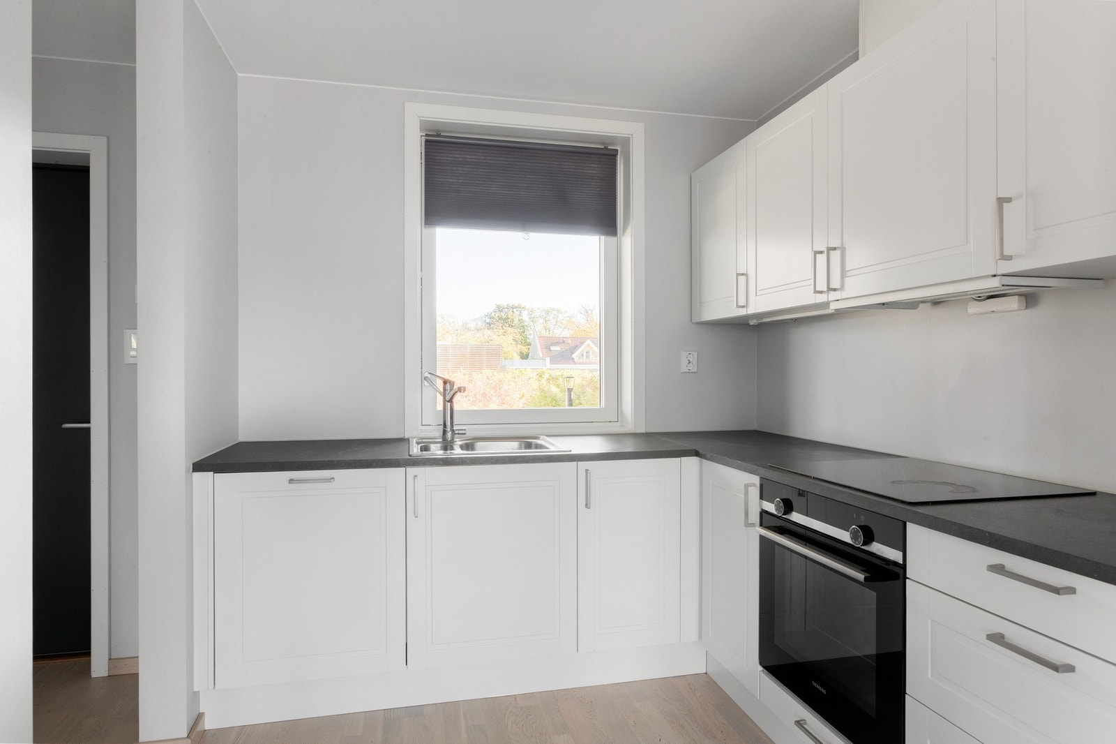 Stilrent kjøkken med hvite fronter, mørk benkeplate og integrerte hvitevarer Galleribilde