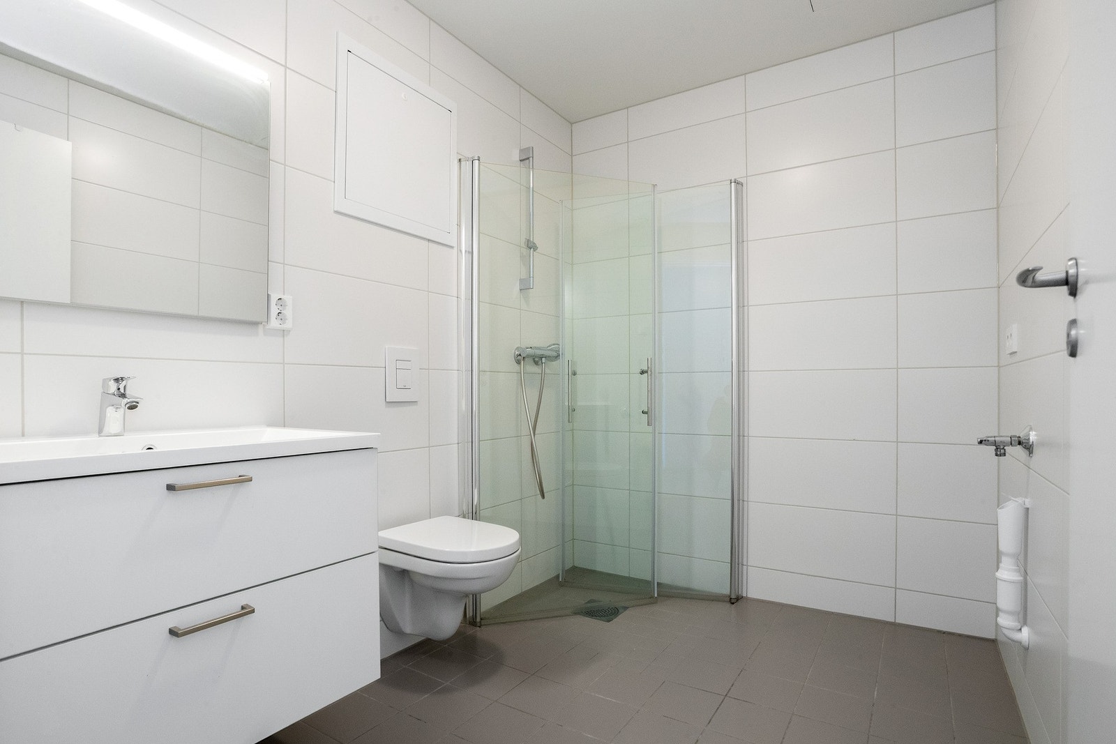 Tidløst, helfliset bad med vegghengt toalett, dusjhjørne og baderomsinnredning med speil og belysning Galleribilde