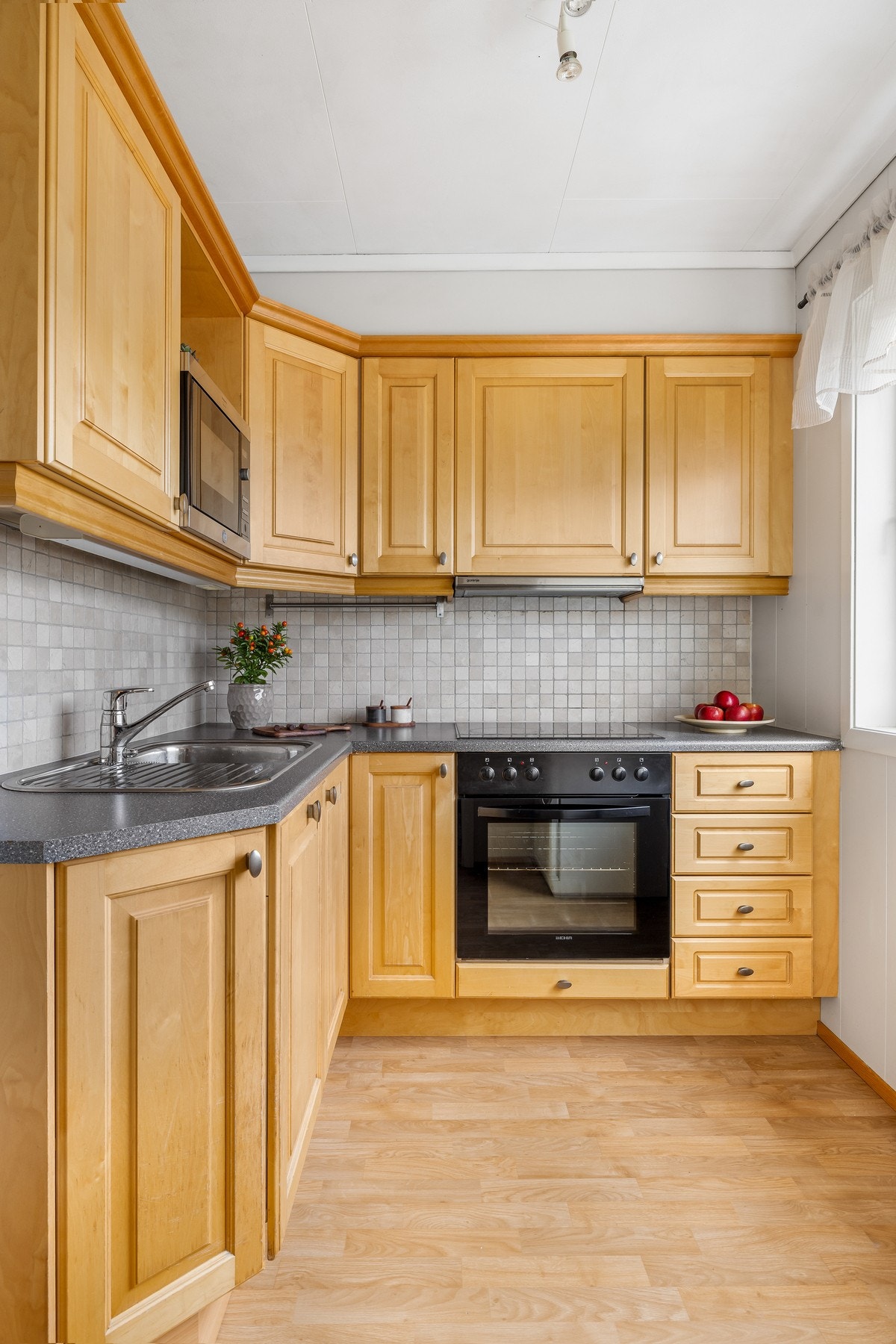 Innredningen har gylne, profilerte fronter og koksgrå laminatbenkeplate med nedfelt kum i stål. Galleribilde