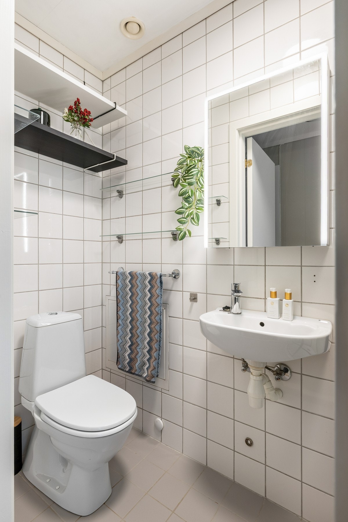 Av innredning er det en vegghengt servant, hyller og et speilskap med belysning, og badet er videre utstyrt med et gulvmontert toalett og et moderne dusjkabinett fra 2023. Galleribilde