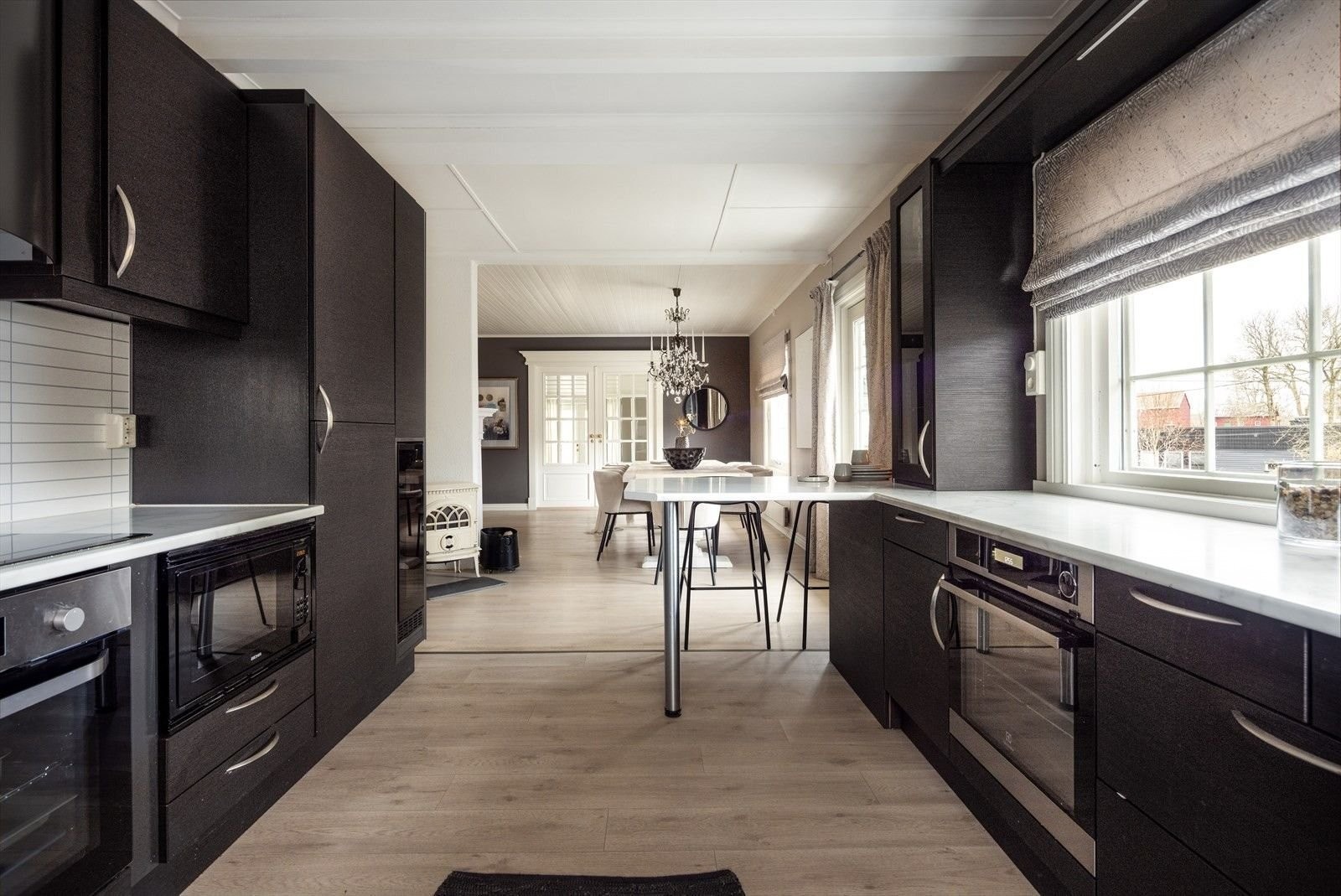 Fra kjøkken mot stue 1: Kjøkken øy med plass til 3 for raske måltider. Spisestuen rommer bord på opptil 3,4 m – perfekt for 12–14 gjester. Fyr i peisen skaper en lun atmosfære. Galleribilde