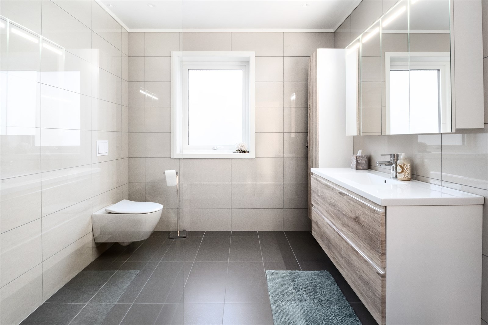 Delikat flislagt baderom med vegghengt toalett, servant med innredning og dusjnisje Galleribilde