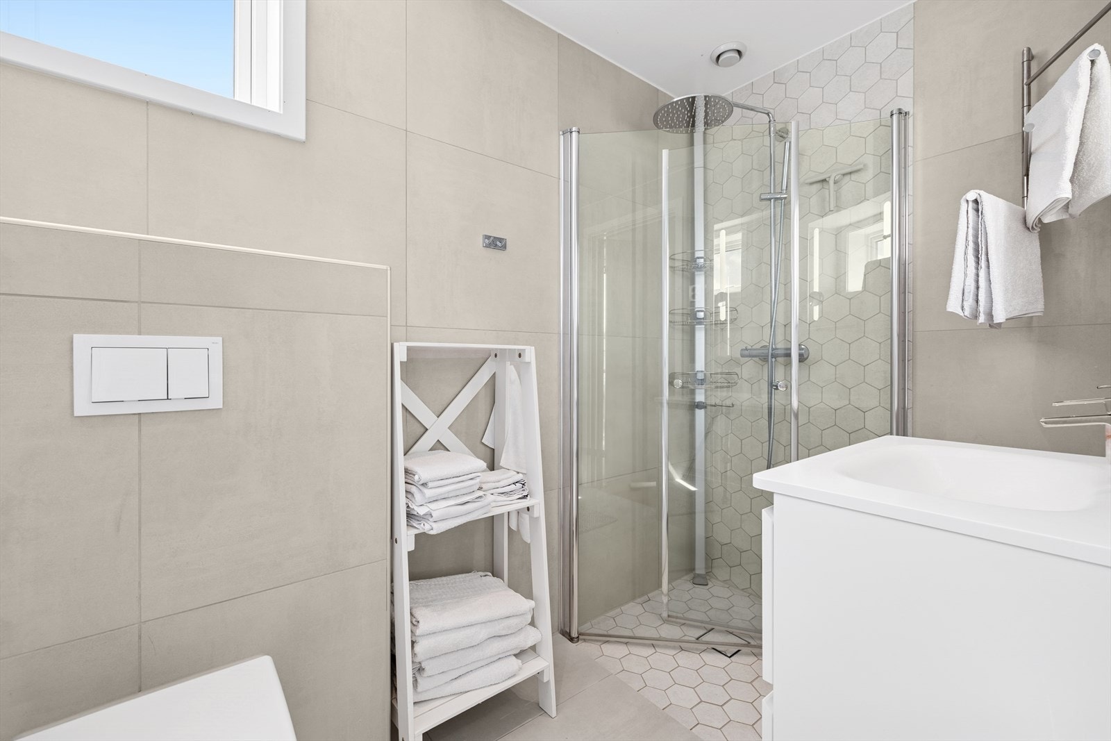 Badet er utstyrt med veggmontert toalett, dusjhjørne og baderomsinnredning med servant. Galleribilde