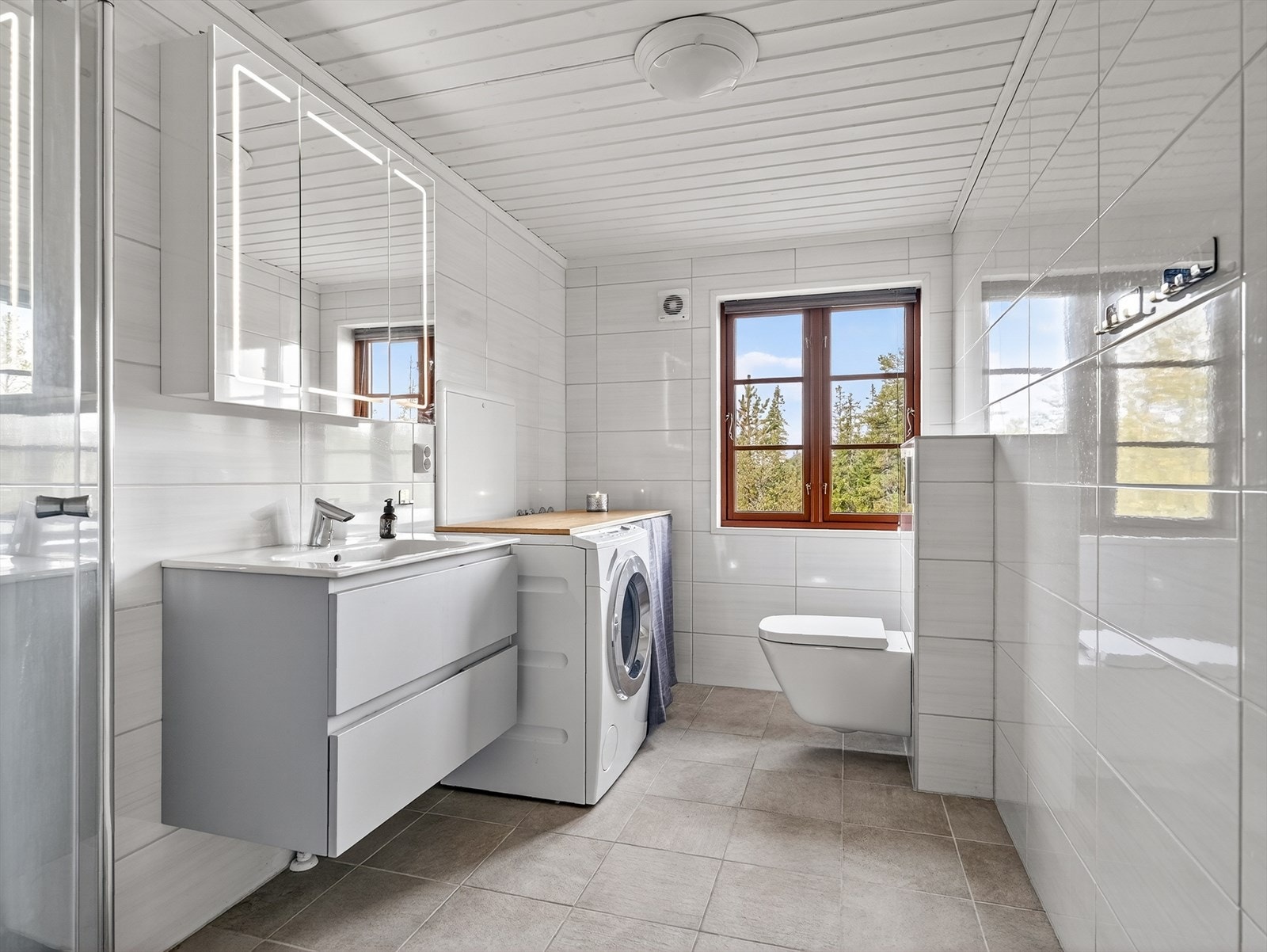 Romslig, flislagt bad med varmekabler i gulv og opplegg for vaskemaskin. Galleribilde