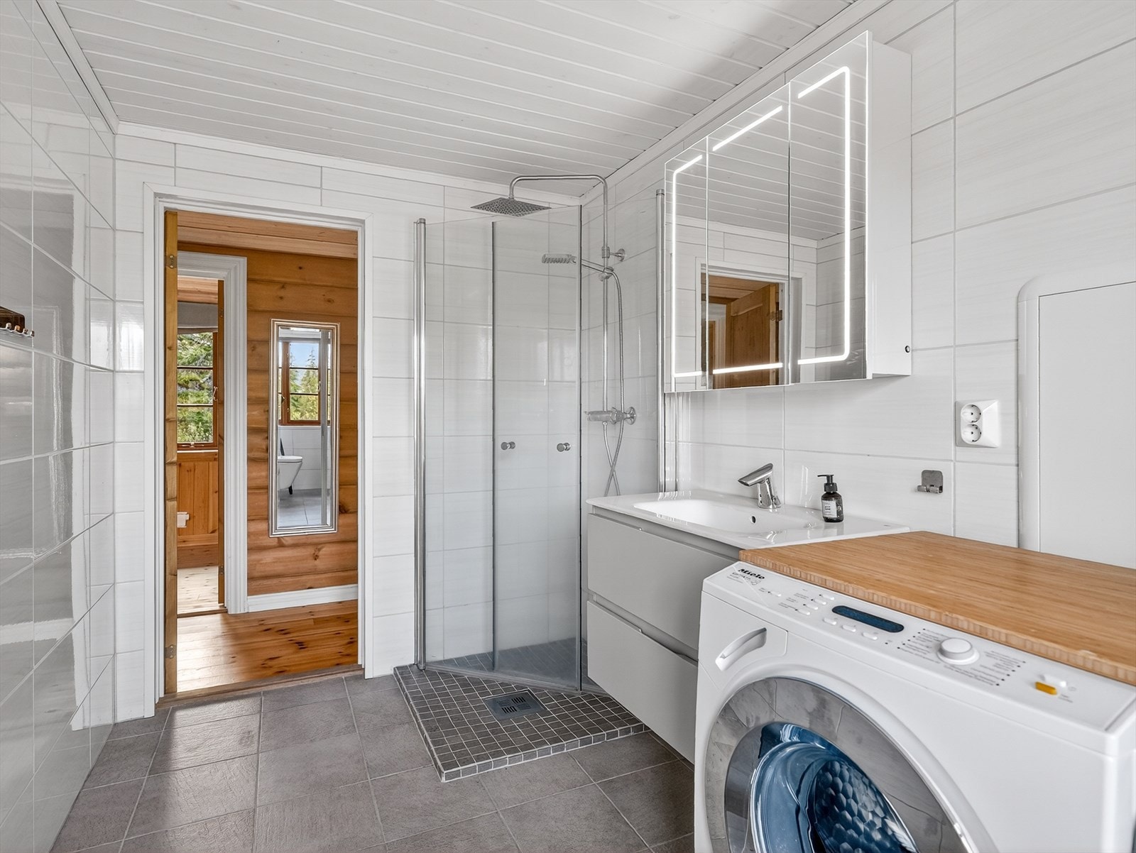 Badet er innredet med veggmontert toalett, dusjhjørne og servantinnredning med skuffer og overskap med speil og lys. Det er elektrisk styrt vifte på vegg. Galleribilde