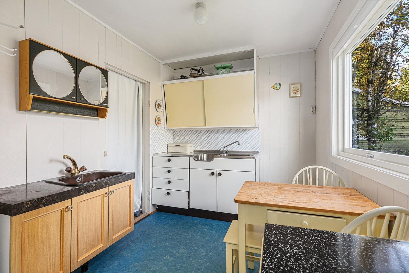 Kjøkkenet har innredning med glatte fronter og overskap med skyvedører fra byggeår og trenger modernisering. Galleribilde