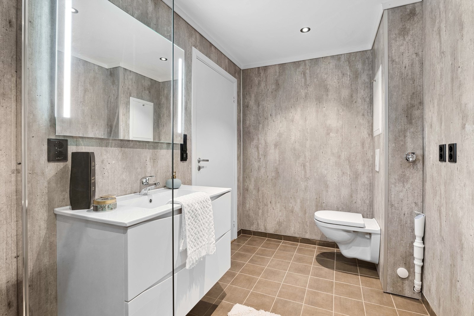 Baderommet har flislagt gulv, baderomsplater på vegger og malt himling med innfelte downlights Galleribilde