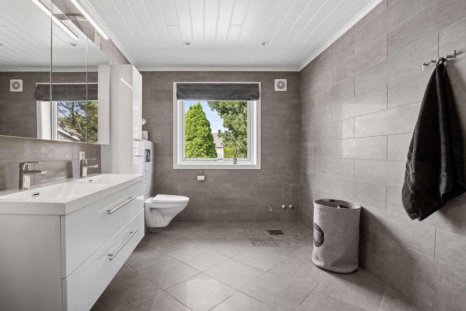 Badet har keramiske fliser på vegger og gulv, med gulvvarme. Himlingen har MDF panel. Rommet er utstyrt med 2 integrerte servanter, veggmontert toalett og dusjvegger/hjørne. Galleribilde