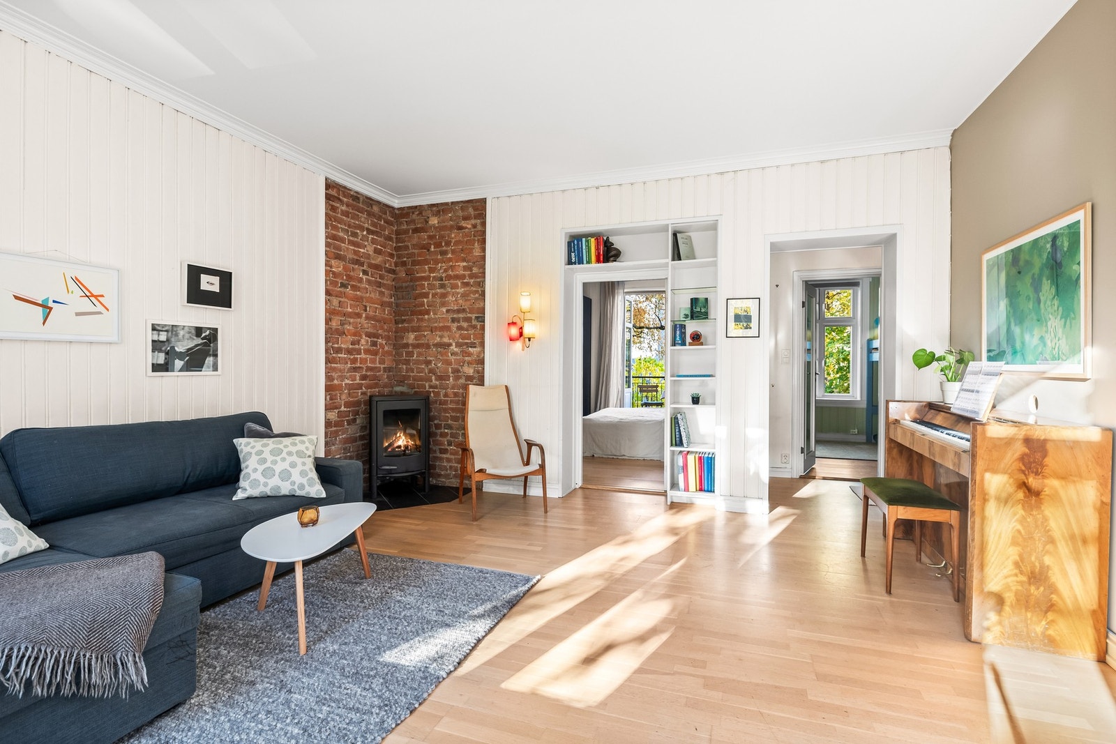 Gulvflater i parkett og fliser ved ildsted gir et tidløst uttrykk, mens veggene består av malte flater, panel og teglstein som tilfører varme og karakter. Galleribilde