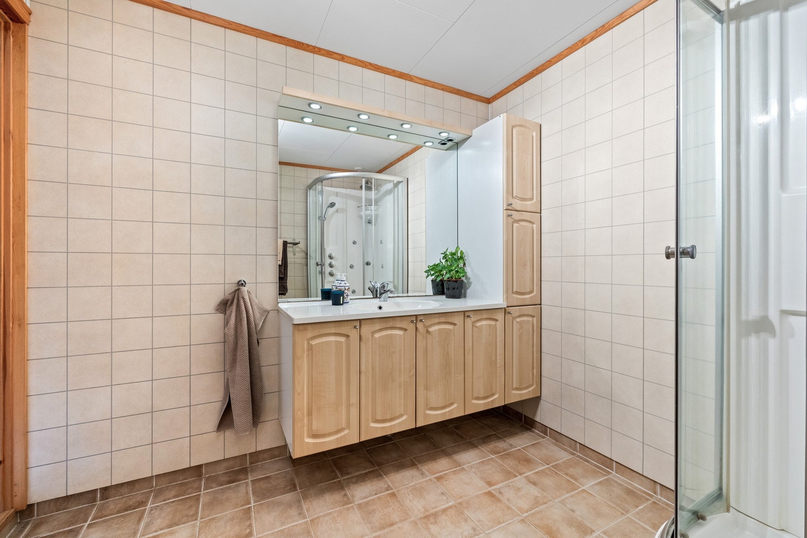 Badet har flislagt gulv med elektrisk gulvvarme, baderomsplater på vegg og vegghengt servantskap med heldekkende servant med ett-greps armatur, høyskap for ekstra lagring. Galleribilde