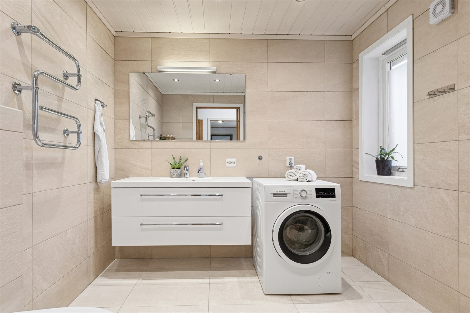 Gulv og vegger er med fliser, og himlingen er med malte plater. Badet er utstyrt med vask, vegghengt klosett, dusjhjørne og det er avløp til vaskemaskin. Galleribilde