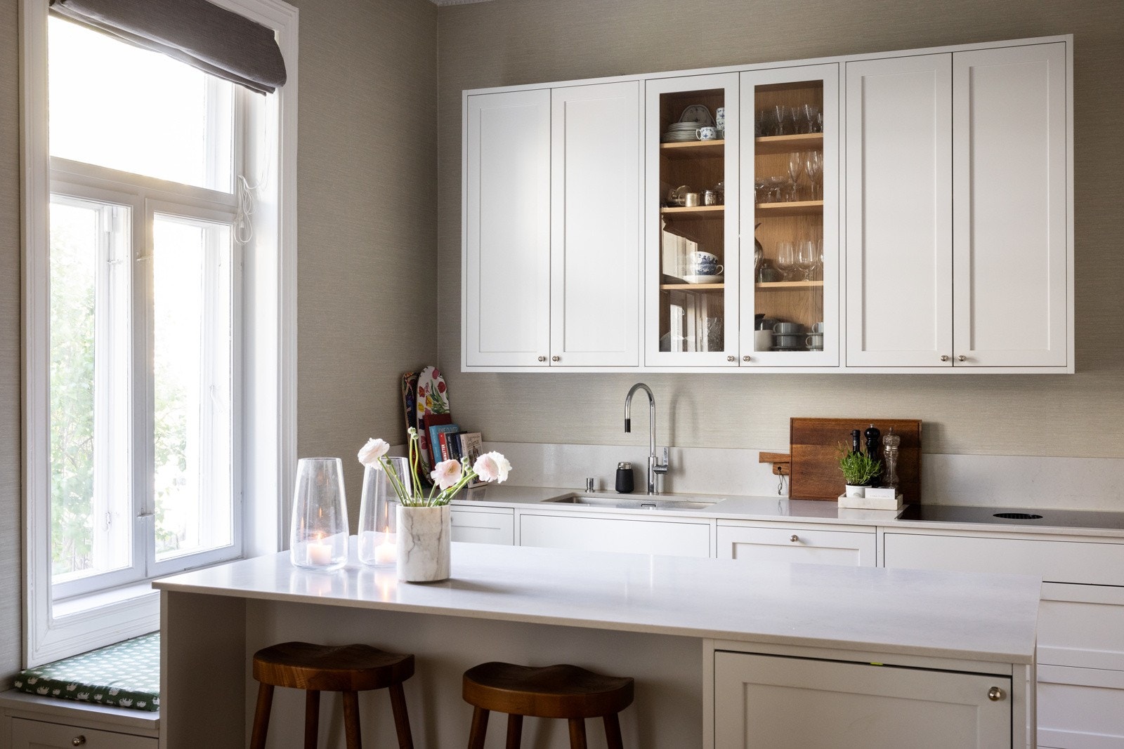 Innredningen består av grå, profilerte fronter kombinert med delikate inndelinger i eikfiner i både skuffer og skap. Belysningen er stilfullt integrert i overskap og over benkeflaten