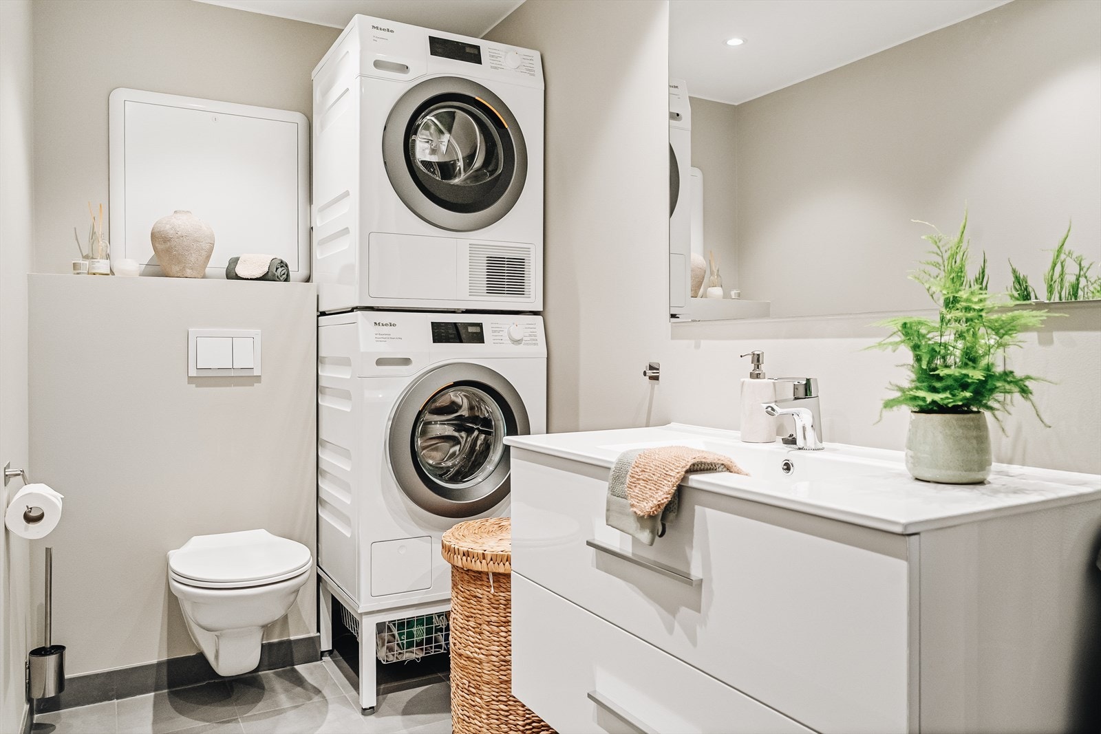 Det andre badet på 4,7 m² er utstyrt med vegghengt toalett, servant og opplegg for både vaskemaskin og tørketrommel. En smart løsning som gir deg egen vaskesone i leiligheten - praktisk både for familier og par som ønsker en effektiv hverdag. Galleribilde