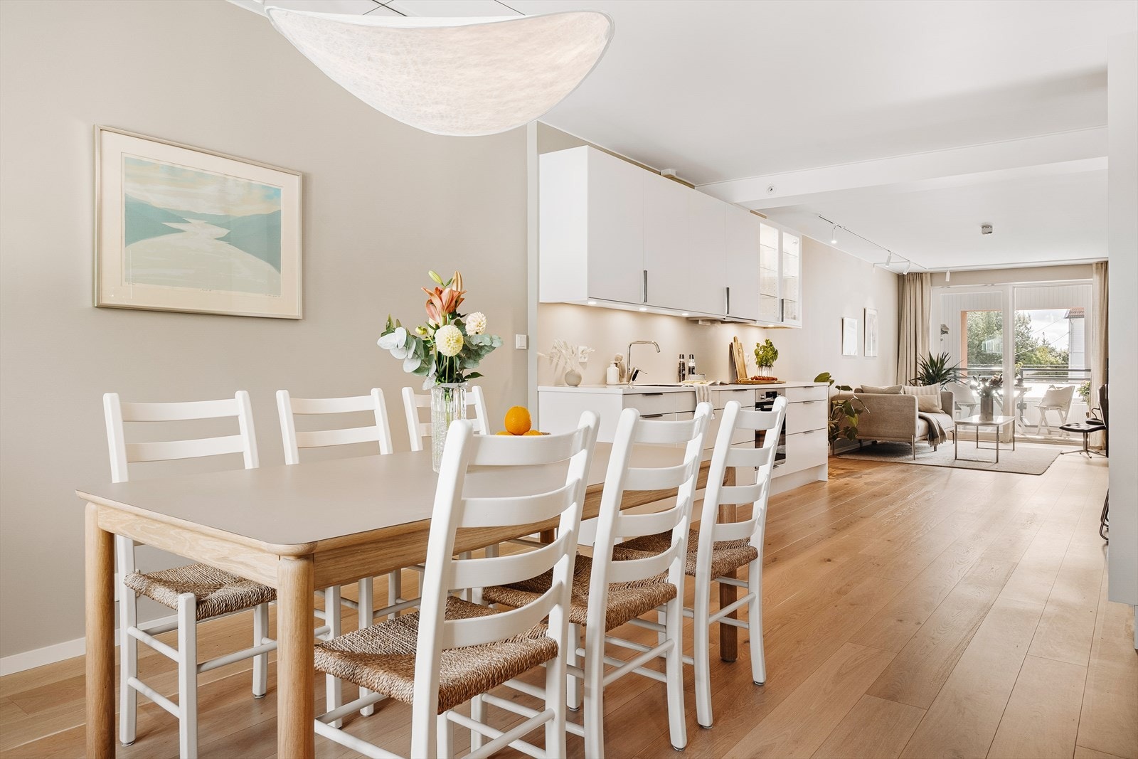 Den åpne løsningen mellom kjøkken og stue gir rom for en stor spiseplass som blir selve hjertet i boligen. Her samles familie og venner til alt fra hverdagsmiddager til festlige lag. Galleribilde