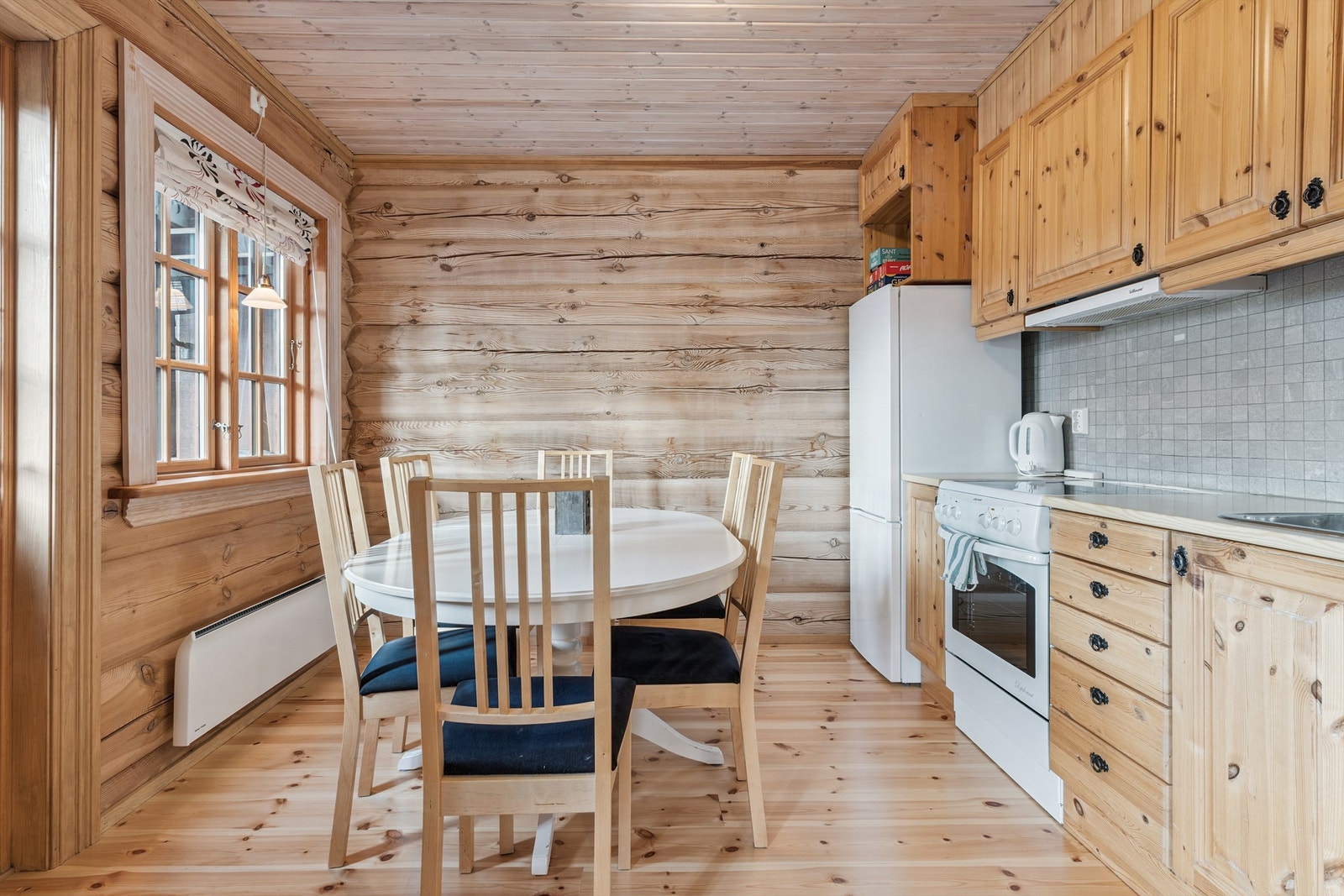 Kjøkkenet har en funksjonell innredning i furu med profilerte fronter og en benkeplate i laminat med nedsenket vask. Galleribilde