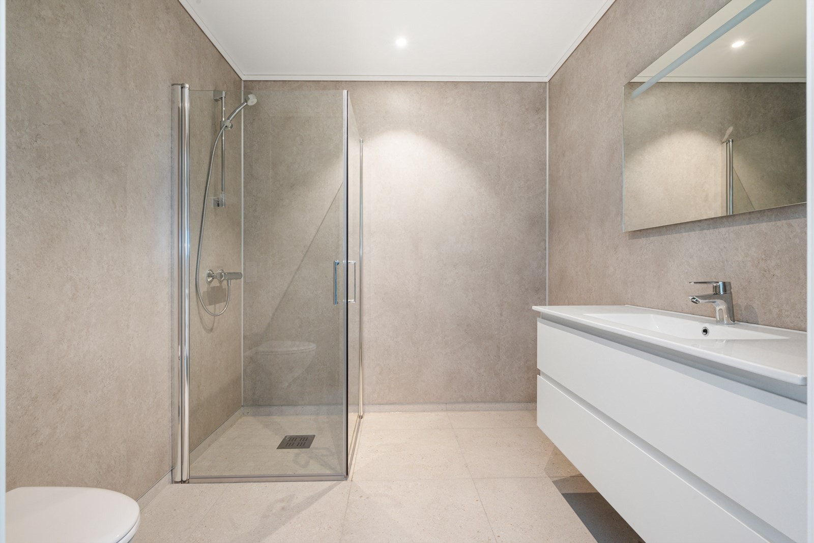 Bad med flis på gulv ilagt varme og våtromsplater på vegger. Malt overflate og downlights i himling. Galleribilde