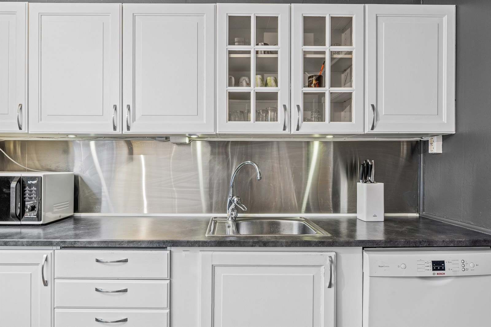 Innredningen er av laminerte skrog, profilerte hvite fronter og laminert benkeplate med nedfelt oppvaskkum i stål Galleribilde