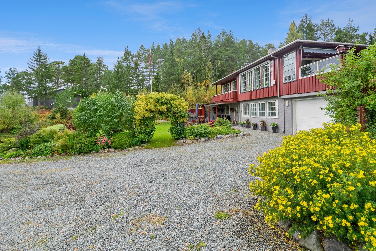 Boligens eiendom bugner av ulike busker, blomster og trær. Boligen har også en garasje med direkte adkomst fra sokkel. Galleribilde