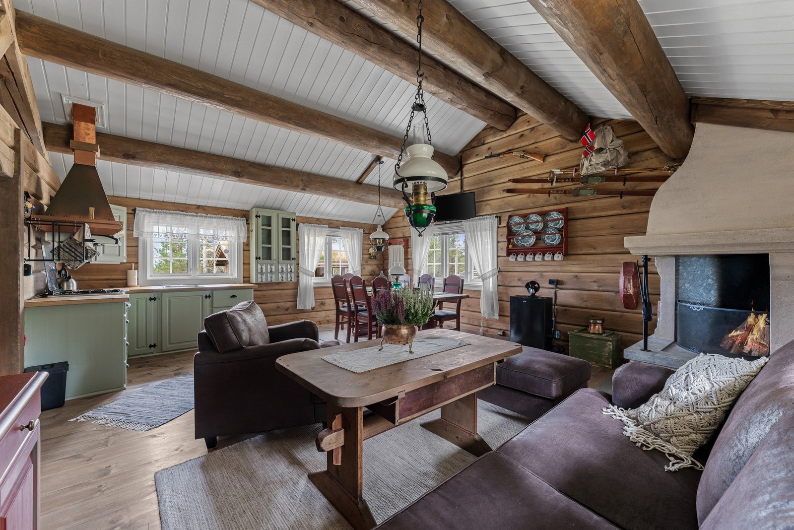 Stuen er selve hjertet i hytta - et lunt samlingspunkt med mektige tømmervegger, hvitmalte himlinger og synlige bjelker som understreker hyttas solide konstruksjon. Galleribilde