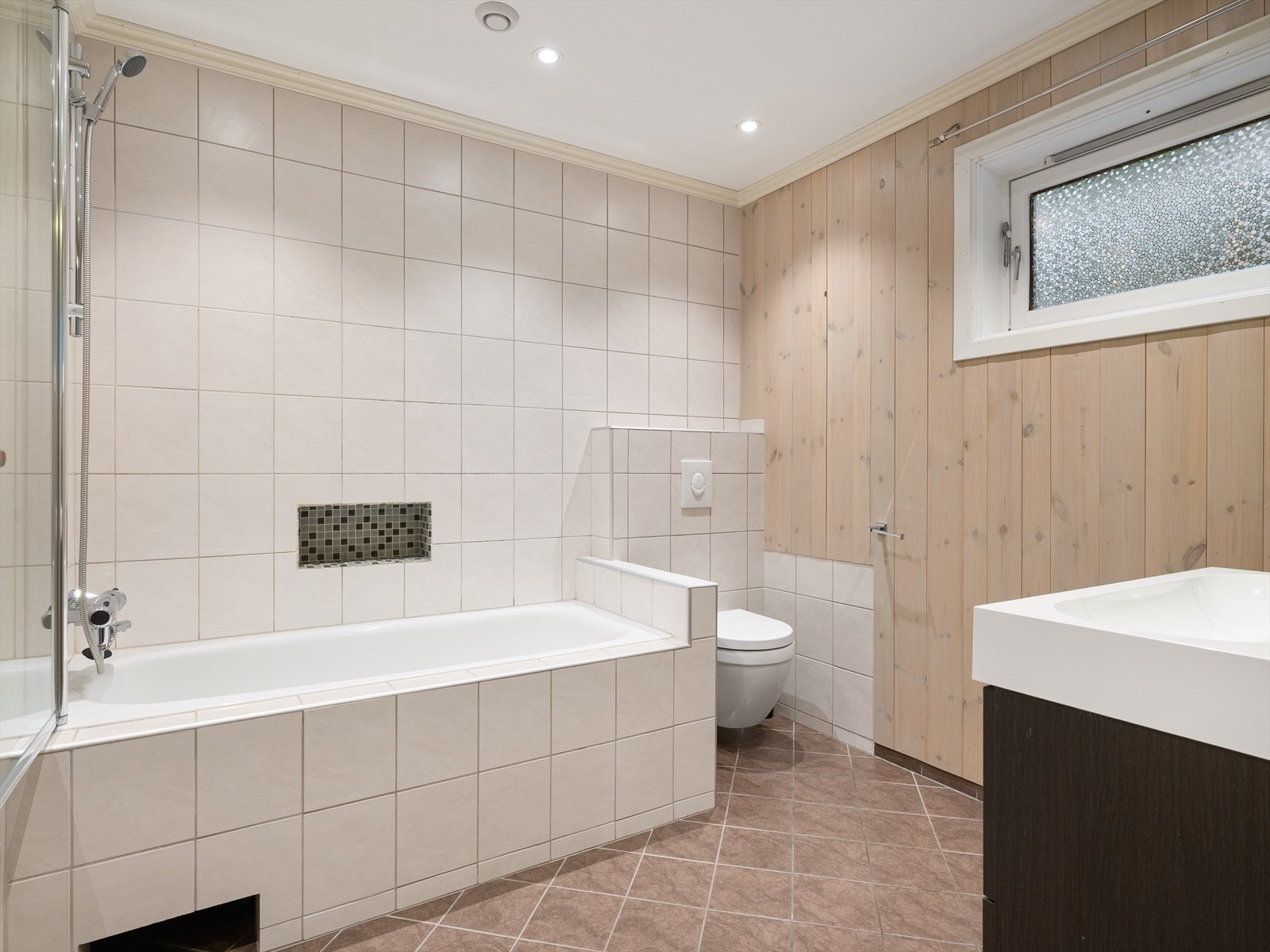 Bad med fliser på gulv og i våtsonen på vegg. Innfliset badekar med dusj. Vegghengt wc og vask i seksjon. Varme i gulv. Spotter i tak. Galleribilde