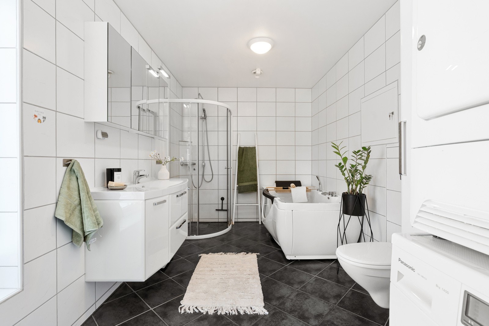 Stort og pent flislagt baderom med opplegg for vaskemaskin som gir enkelhet og bekvemmelighet i hverdagen. Galleribilde