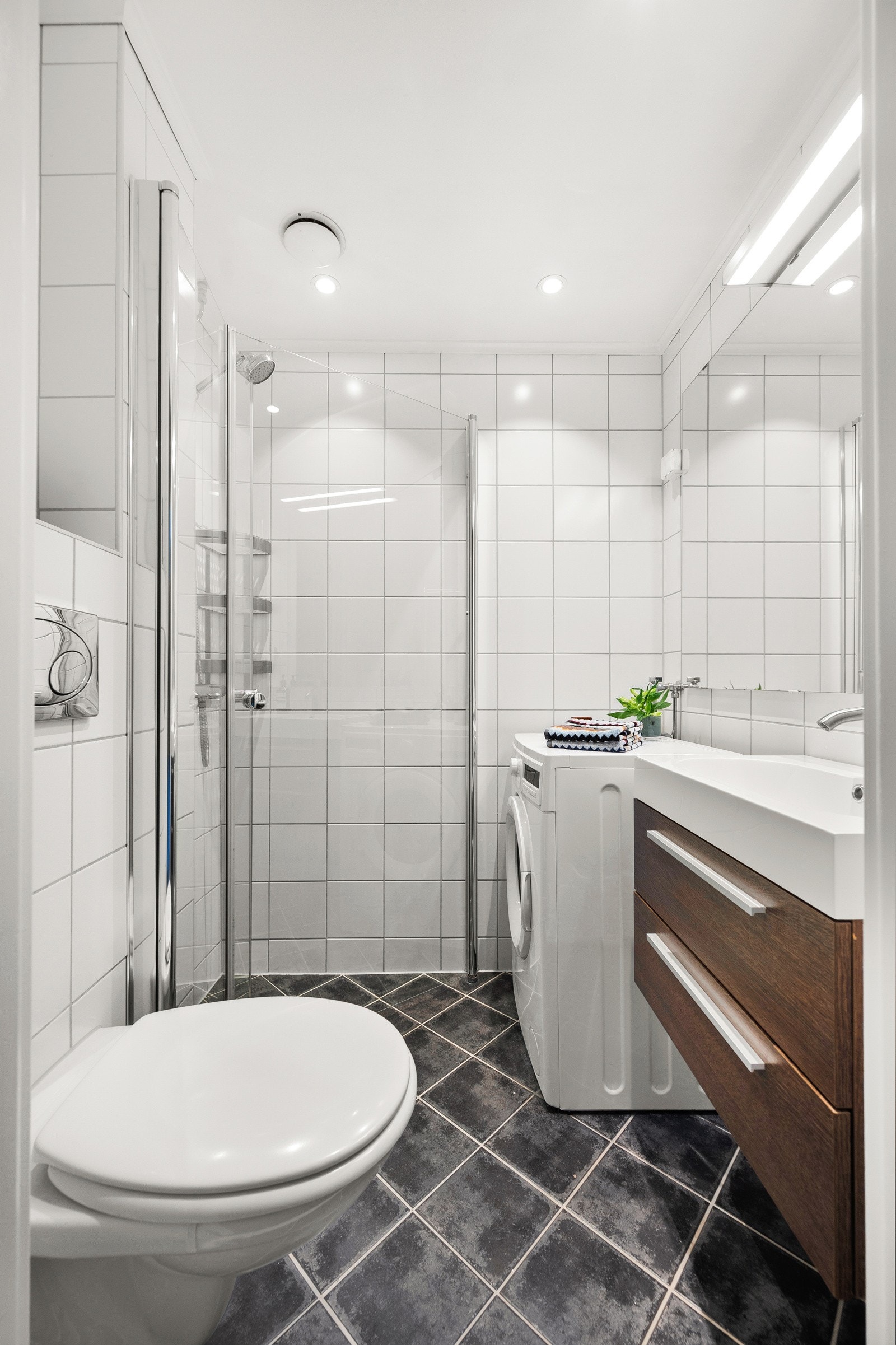 Pent baderom med vegghengt toalett, dusjhjørne med to svingbare glassdører, servant med slette fronter og oplegg for vaskemaskin. Badet ble pusset opp i regi av borettslaget i 2008. Galleribilde