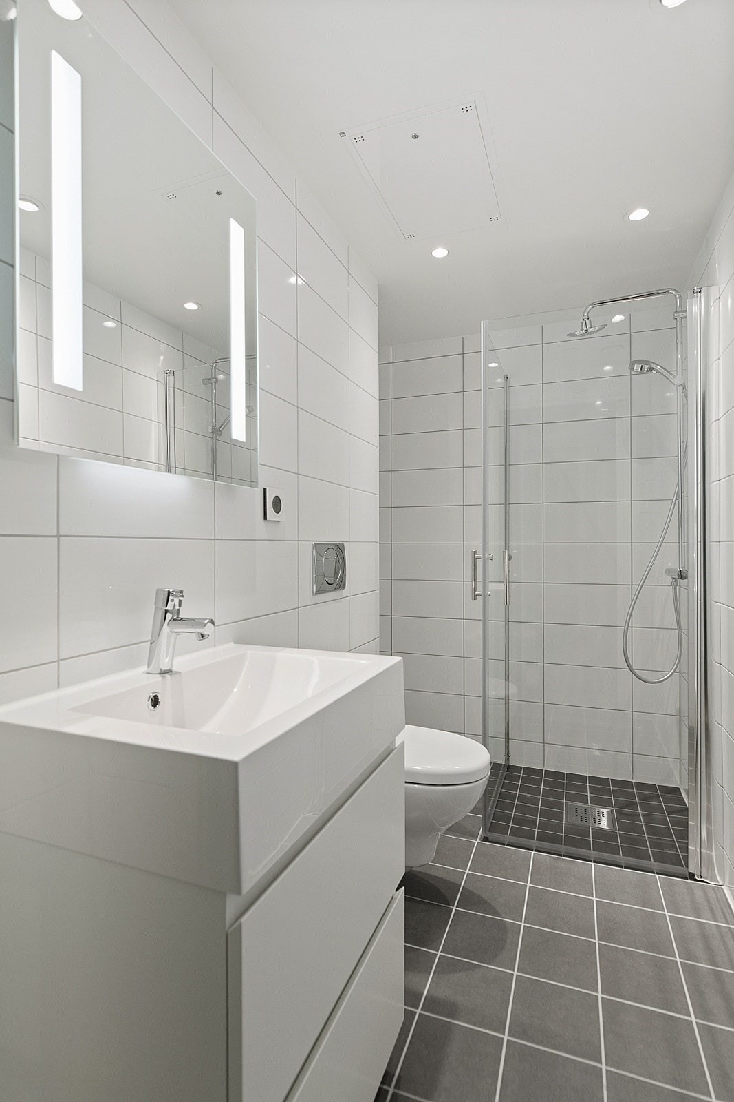 Badet fremstår som meget flott og stilrent, med grå fliser på gulvet og store, hvite fliser på veggene. Gulvvarme gir ekstra komfort og rommet er utstyrt med opplegg for vaskemaskin. Galleribilde