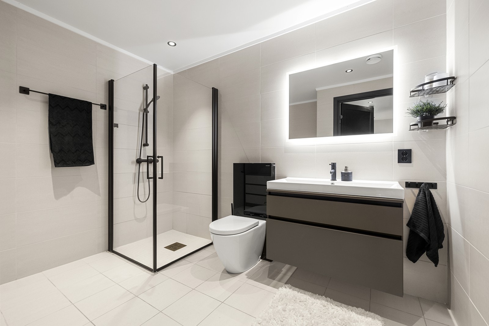 Baderommet er stilrent med lyse fliser på vegger og gulv med sorte detaljer på innredningen. Galleribilde
