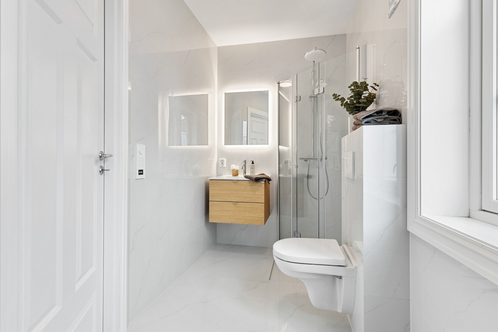 Delikat baderom innredet med vegghengt toalett, dusjhjørne med glassvegger og innredning med nedfelt servant Galleribilde