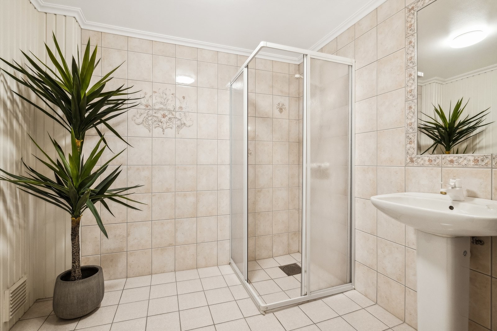 Bad i kjelleretasje med flis på gulv og 3 av 4 vegger. Panel på vegg med inngang til badstue. Galleribilde