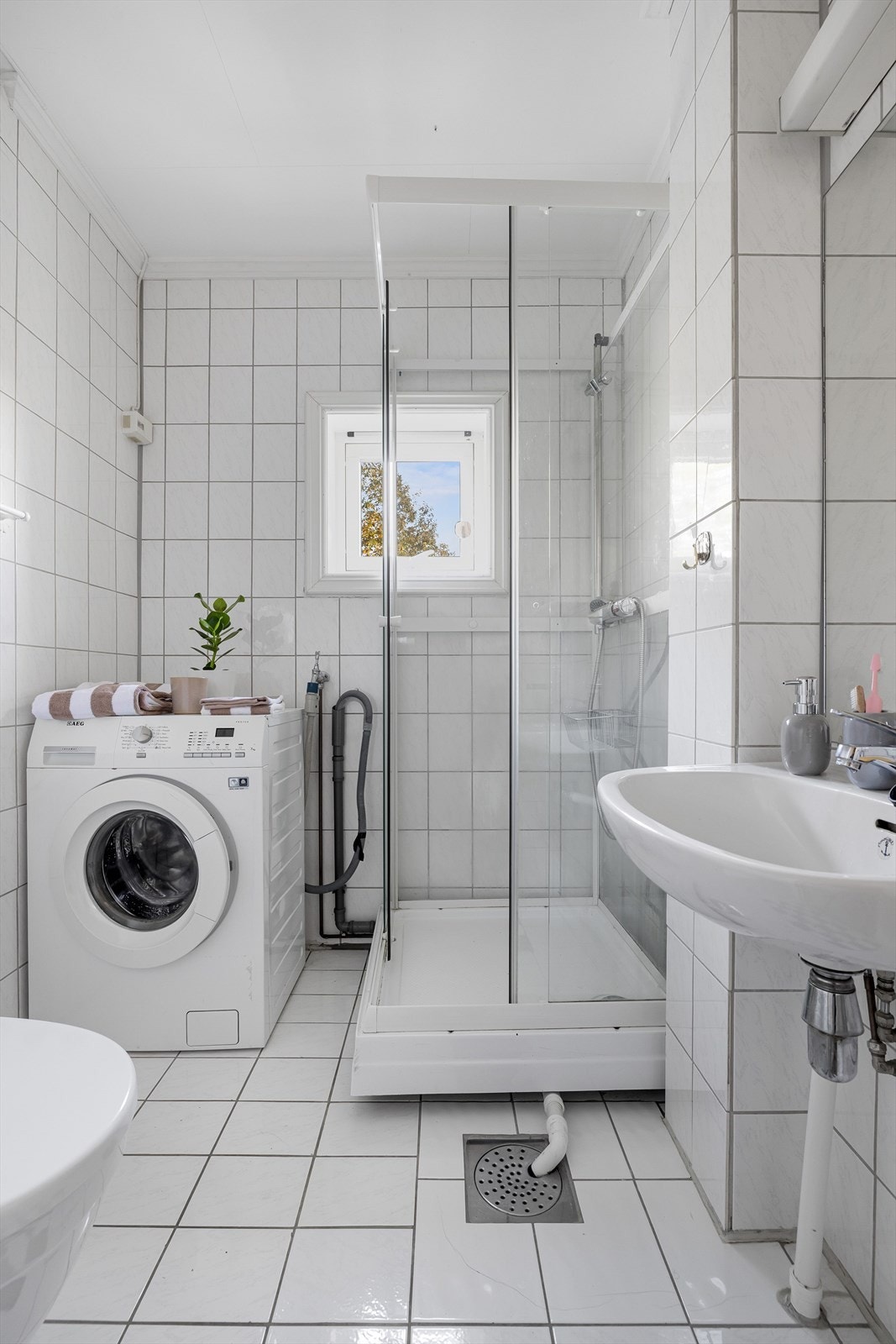 Baderommet er utstyrt med vegghengt servant med speil og belysning over, dusjkabinett og gulvstående toalett. I hjørnet er det plass og opplegg for vaskemaskin. Galleribilde