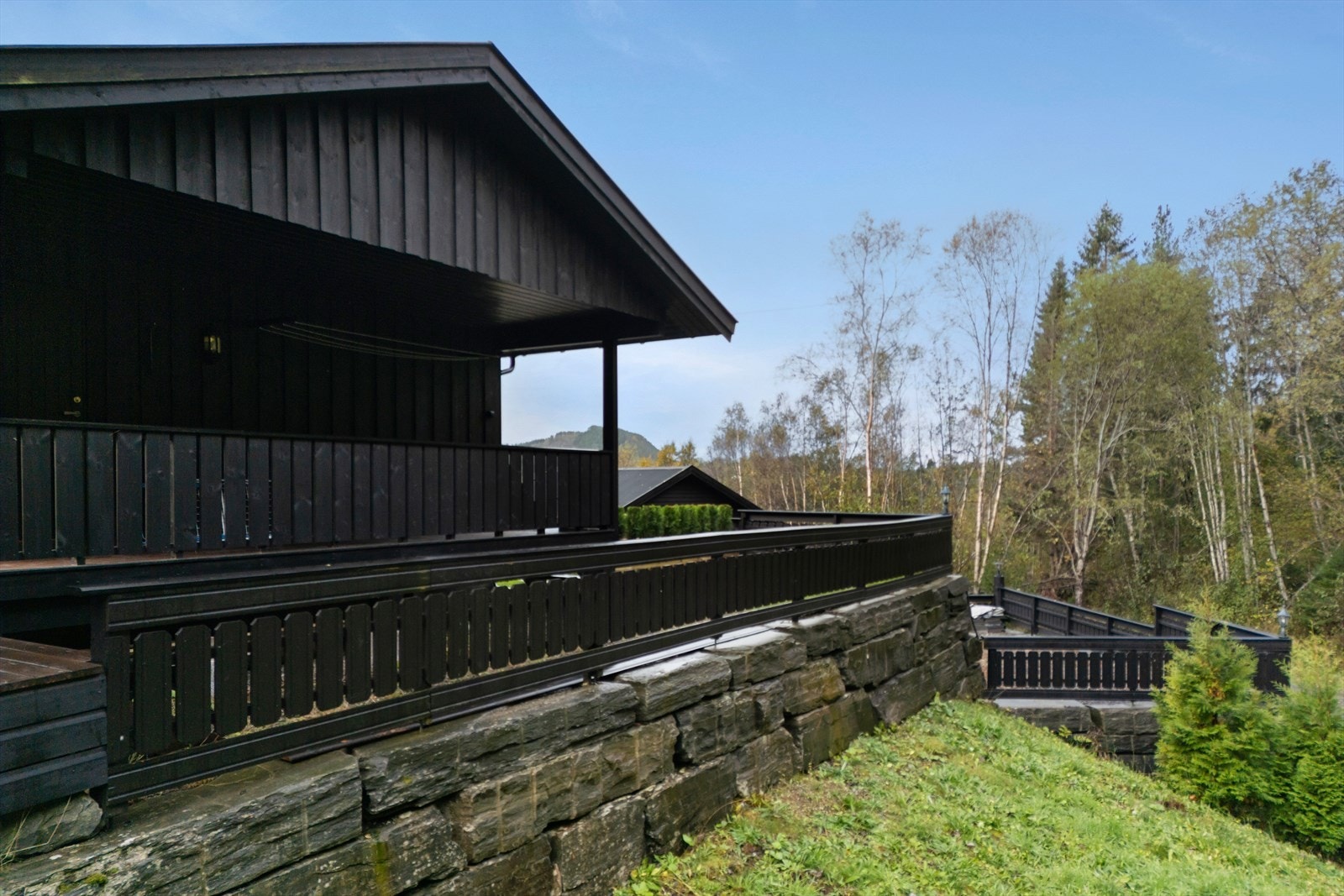 Verandaen er bygget med terrassebord og har rekkverk i en kombinasjon av glass og vertikale spiler. Galleribilde